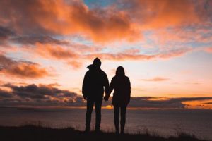 couple holding hands looking at sunset